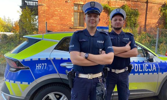 Dwaj umundurowani policjanci ruchu drogowego stoją przed radiowozem.