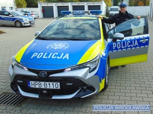 POLICJANT STOI PRZY RADIOWOZIE.