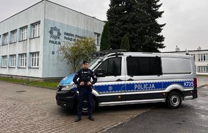 Umundurowany policjant stoi przed policyjnym furgonem.