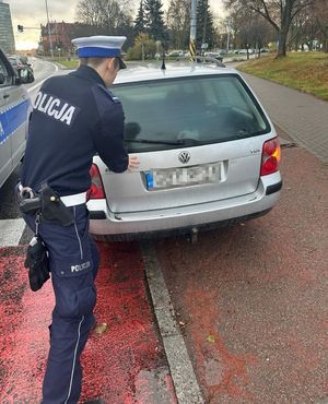 Policjant przy zepsutym samochodzie w kolorze szarym.