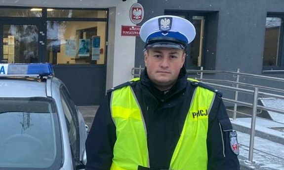 policjant stoi obok radiowozu.