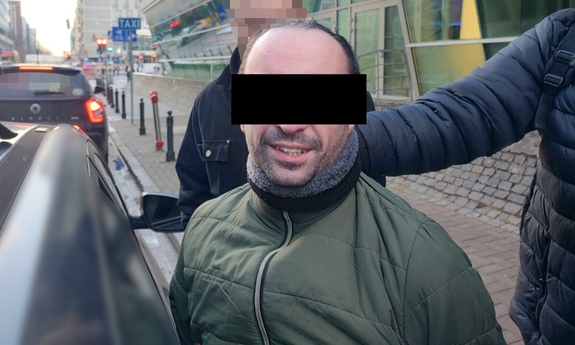 Funkcjonariusz z zatrzymanym mężczyzną przy radiowozie.