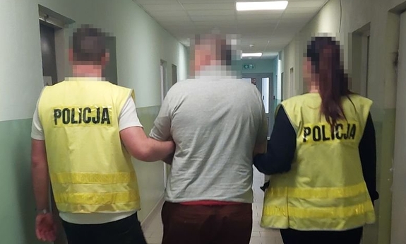 Funkcjonariusze prowadzą korytarzem zatrzymanego mężczyznę zakutego w kajdanki.