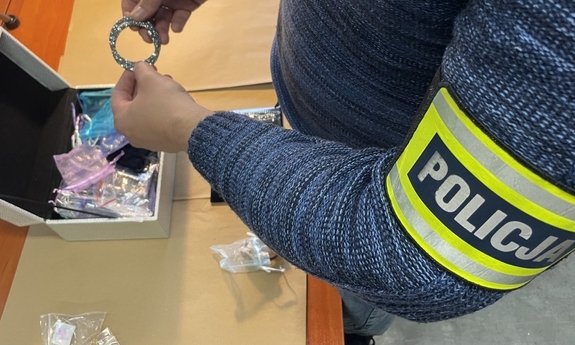 Na zdjęciu opaska policja na ramieniu oraz biżuteria trzymana przez policjanta.