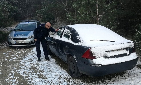 Zdjęcie przedstawia radiowóz oraz policjanta zerkającego przez szybę do pojazdu osobowego.