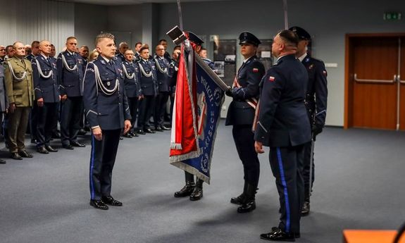 policjant stoi przed sztandarem.