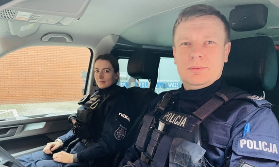 Policjant i policjantka siedzą w radiowozie policyjnym.