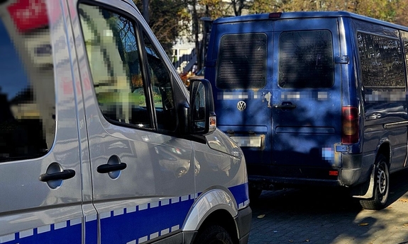 Radiowóz i stojący przed nim niebieski bus.