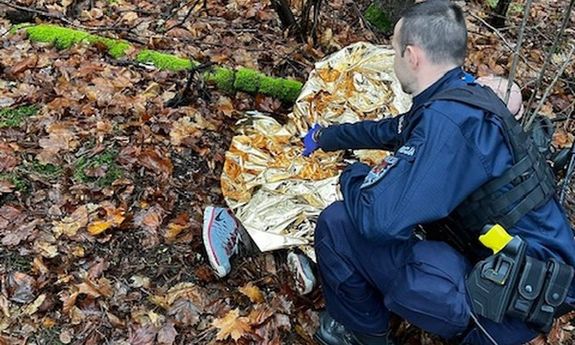 las, na ziemi leży mężczyzna okryty przez policjanta kocem.