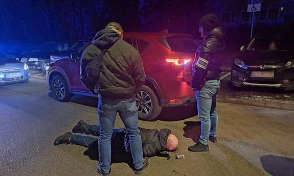Na zdjęciu policjanci stoją nad zatrzymanym mężczyzną, w tle odzyskany samochód z kradzieży.