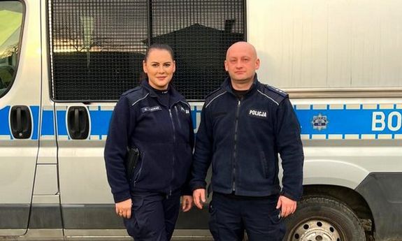 policjant i policjantka stoją przed radiowozem.