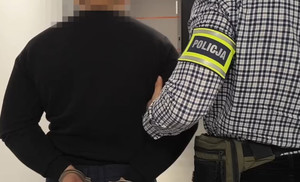 Policjant z zatrzymanym zakutym w kajdanki.