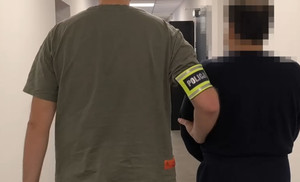 Policjant z zatrzymanym zakutym w kajdanki.