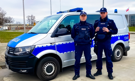Dwóch umundurowanych policjantów stoi przy radiowozie.