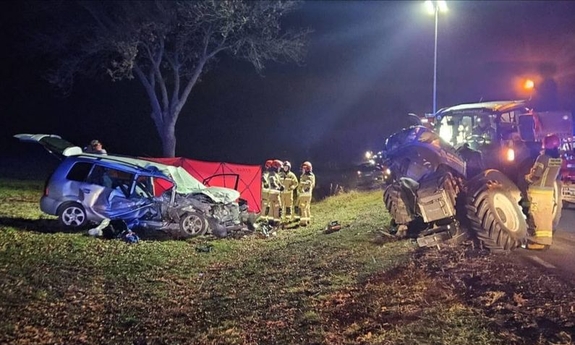 Miejsce wypadku. Uszkodzony samochód osobowy i traktor. Przy rozbitym samochodzie strażacy.