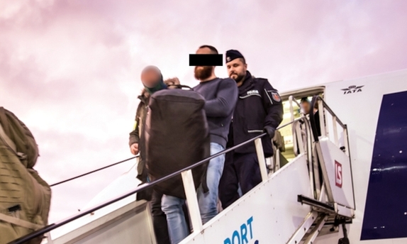 Policjanci wyprowadzają z samolotu zatrzymanego mężczyznę.