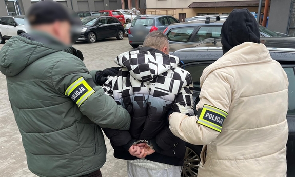 Funkcjonariusze z zatrzymanym mężczyzną przy nieoznakowanym radiowozie.