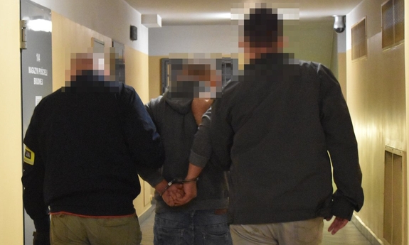 Policjanci z zatrzymanym mężczyzną w kajdankach.