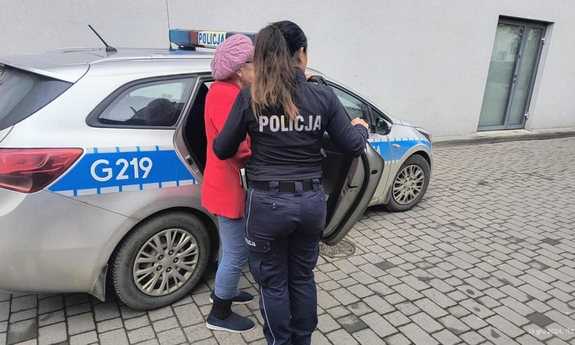 Umundurowana policjantka i starsza kobieta stoją przy radiowozie.