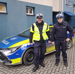 policjanci stoją obok radiowozu.