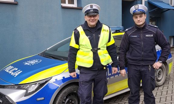 policjanci stoją obok radiowozu.
