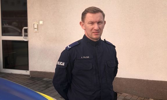 policjant stoi przy radiowozie.