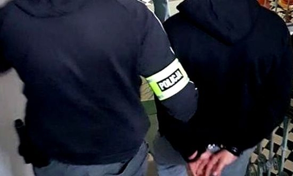 Funkcjonariusz prowadzi zatrzymanego mężczyznę.