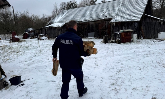 Na zdjęciu umundurowany policjant niesie drewno do domu.