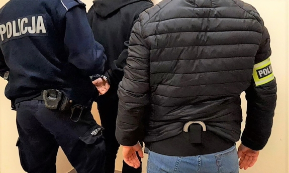 Dwóch policjantów prowadzi zatrzymanego mężczyznę.