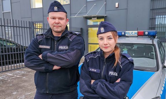 policjanci stoją przed radiowozem.
