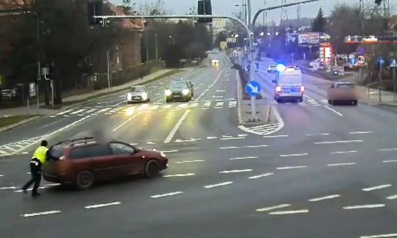 kadr z monitoringu. policjant pomaga pchać samochód.