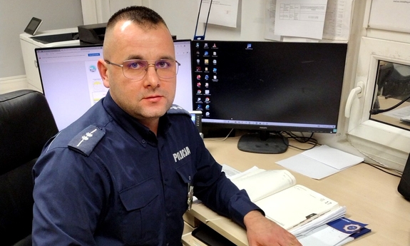 Na zdjęciu umundurowany policjant siedzi przy biurku.