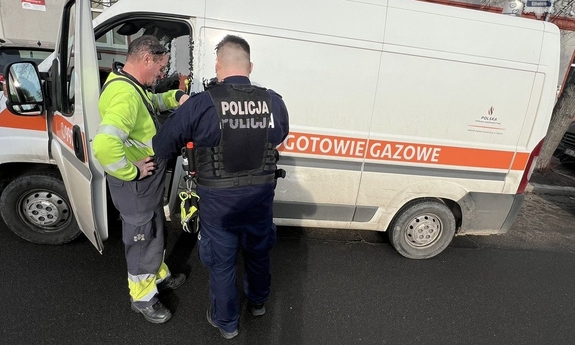 Policjant rozmawiający z pracownikiem gazowni przy charakterystycznym samochodzie pogotowie gazowe.