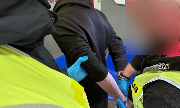 Policjanci zakładają kajdanki na ręce zatrzymanej osoby.