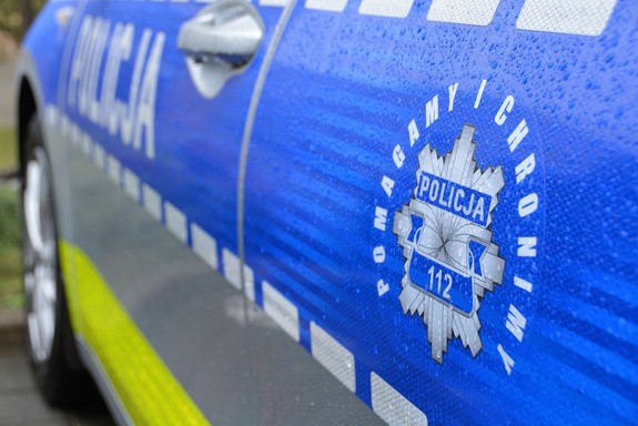Bok policyjnego radiowozu, na którym widnieje napis Policja i policyjna gwiazda a wokół niej napis: Pomagamy i chronimy.