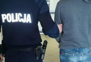 Zatrzymany mężczyzna prowadzony przez policjanta.