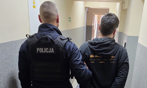 Umundurowany policjant wraz z zatrzymanym mężczyzną na korytarzu.
