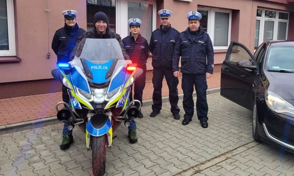 mężczyzna siedzi na policyjnym motocyklu, a obok stoją policjanci.