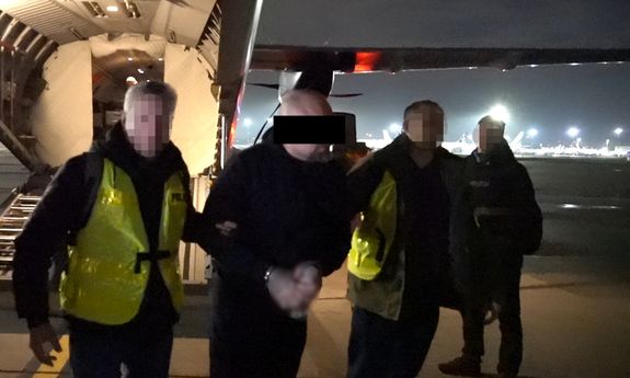 policjanci idą z zatrzymanym po płycie lotniska, w tle widać skrzydło samolotu.