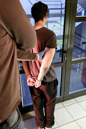 Zatrzymany mężczyzna skuty kajdankami. Z boku widać fragment ciała policjanta w ubraniu cywilnym, który prowadzi zatrzymanego.