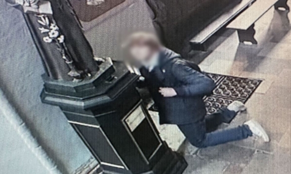 Na zdjęciu mężczyzna usiłuje włamać się do kościelnej skarbony.