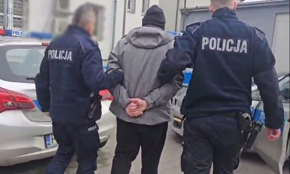 Dwaj funkcjonariusze prowadza zatrzymanego mężczyznę.