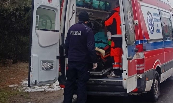 Umundurowany policjant z medykami wprowadzają mężczyznę do karetki.