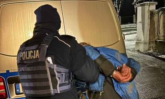 Policjant prowadzi zatrzymanego do radiowozu.