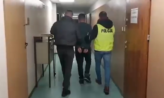 Dwaj funkcjonariusze prowadzą korytarzem zatrzymanego.