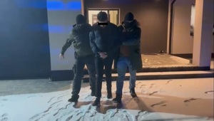 Dwaj funkcjonariusze prowadzą mężczyznę zakutego w kajdanki.