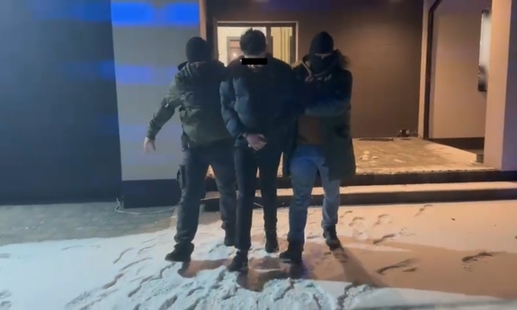 Dwaj funkcjonariusze prowadzą mężczyznę zakutego w kajdanki.
