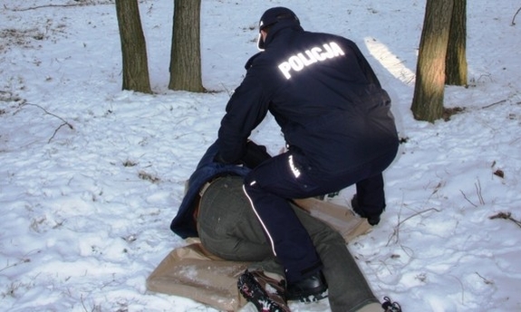 Policjant pomaga osobie leżącej na śniegu.