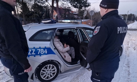 Policjanci stojący przy radiowozie, w którym siedzi odnaleziona kobieta.