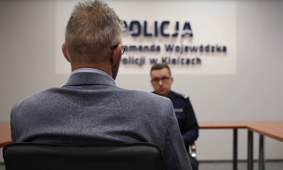 Policjant rozmawia z mężczyzną. Obaj siedzą na krzesłach naprzeciwko siebie.
